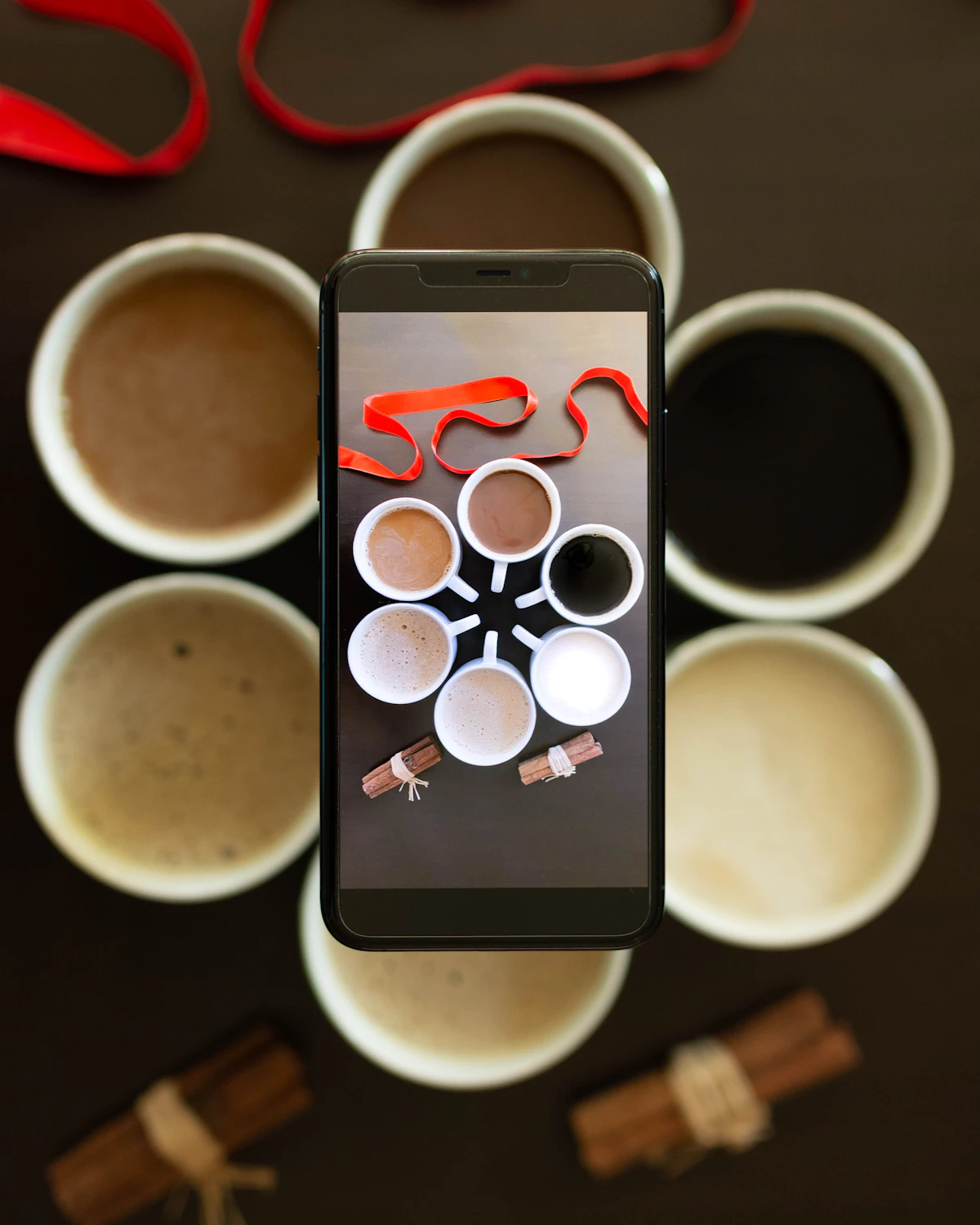 A phone propped against a coffee cup playing a paused how-to video, laptop open in the background