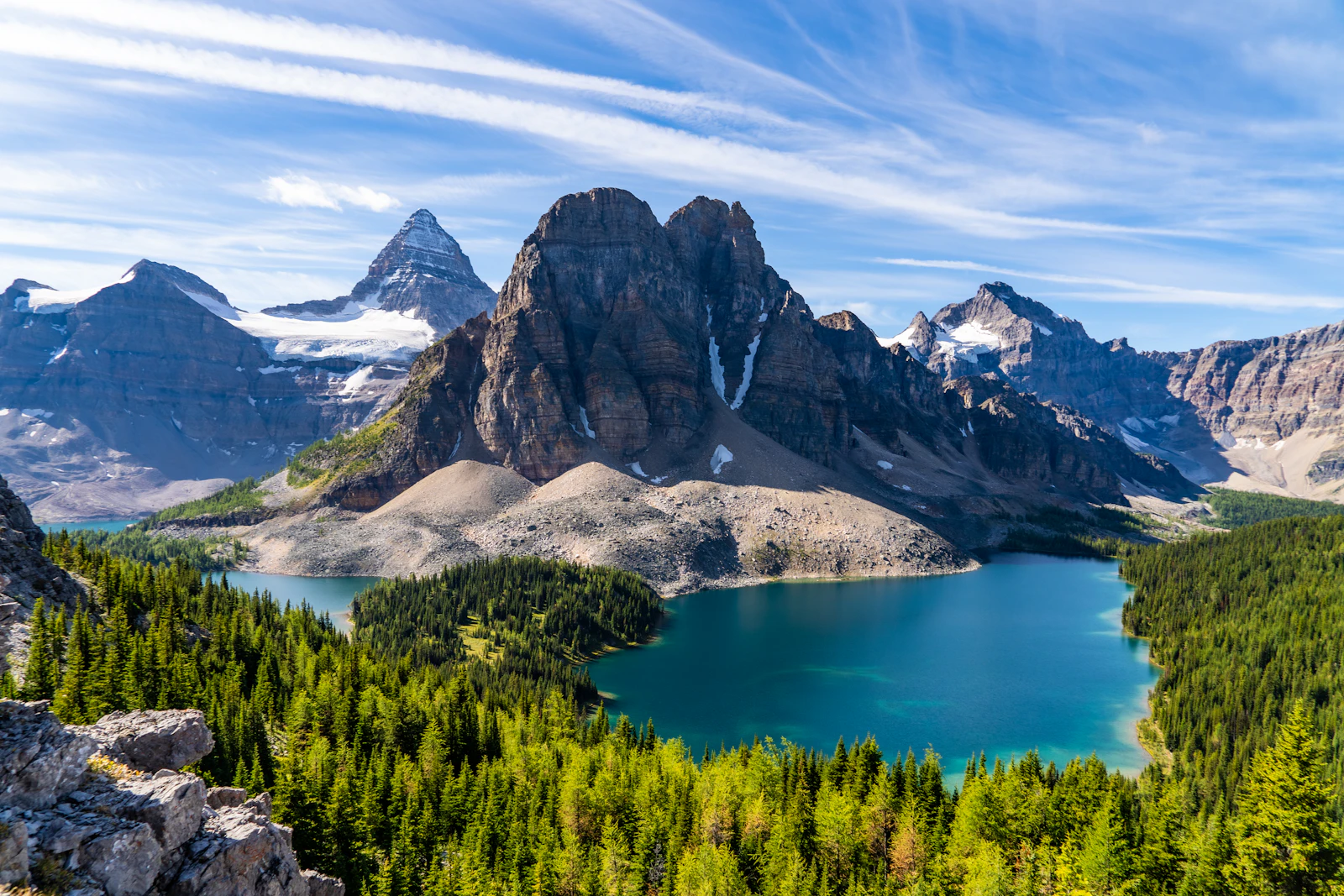 A still Canadian lake ringed by evergreen forest and a long range of mountains under a clear blue sky