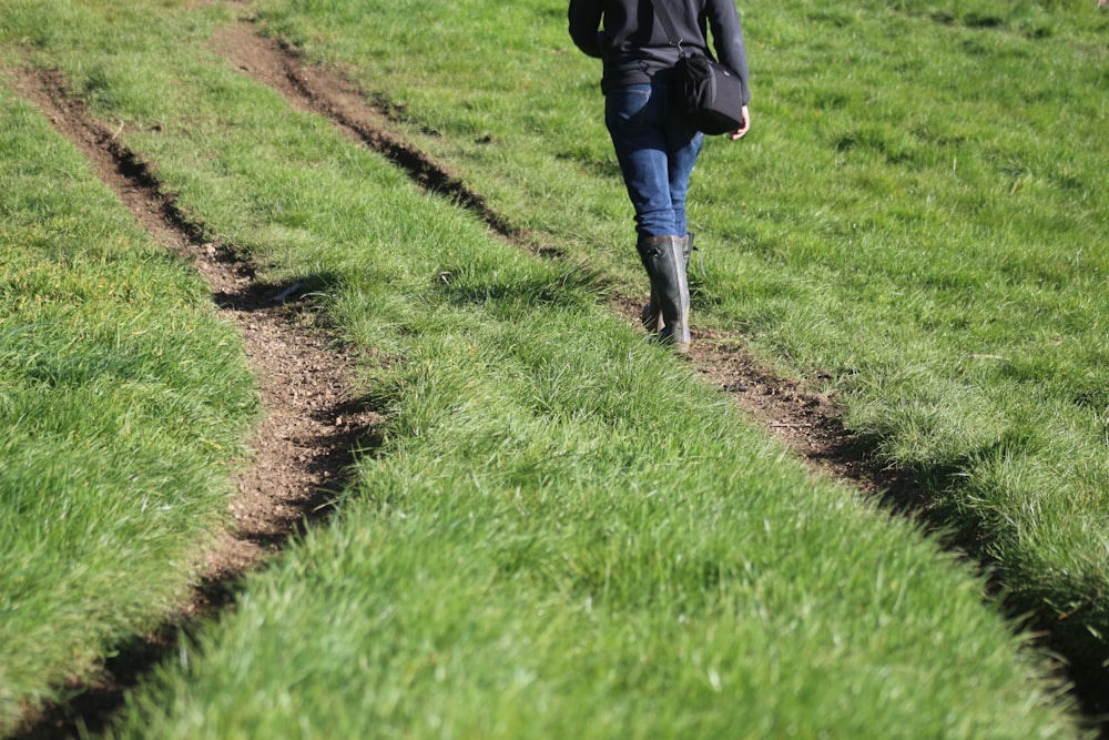 Persona con chaqueta negra caminando en el campo de hierba verde durante el día