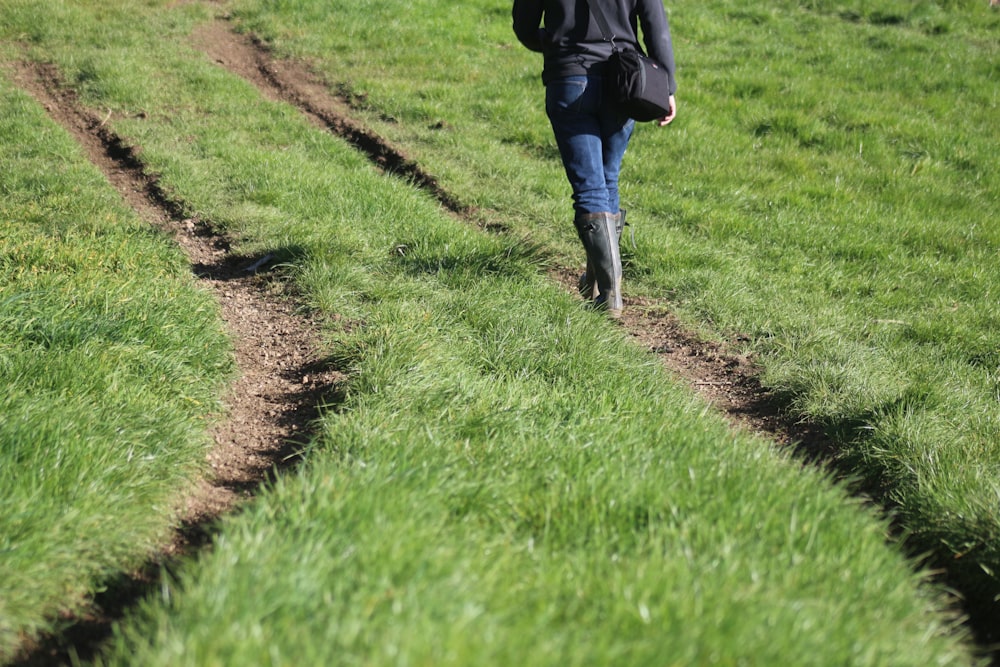 person in black jacket walking on green grass field during daytime