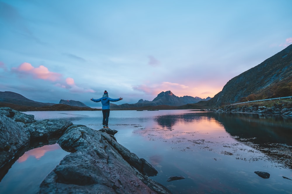 man in black shirt standing on rock near body of water during daytime