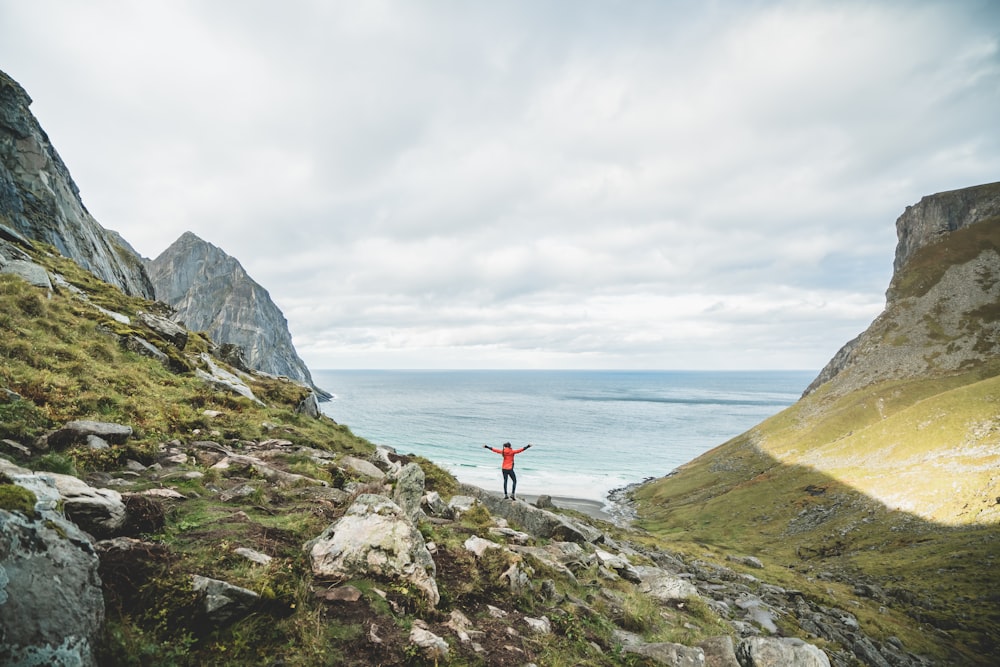 person in red shirt standing on rock near body of water during daytime