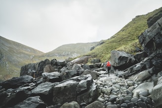 person in red jacket sitting on rock near mountain during daytime