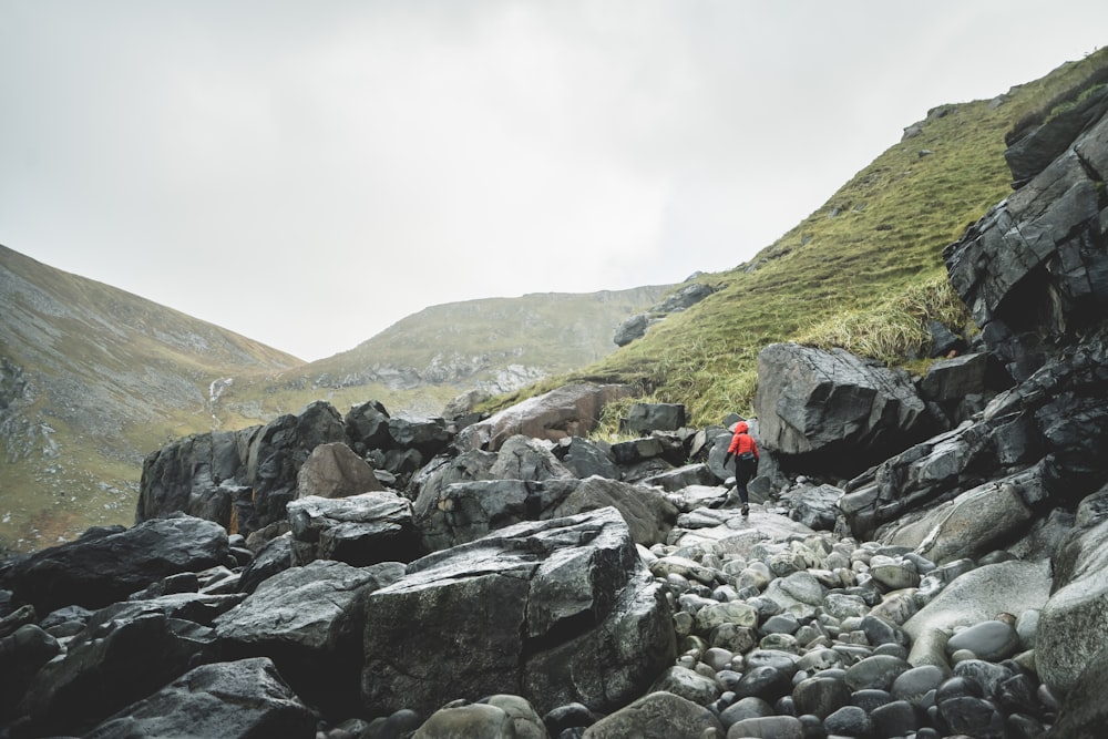 person in red jacket sitting on rock near mountain during daytime