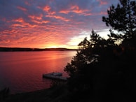 A vibrant sunset reflecting off a calm lake with kayaks resting on the dock.