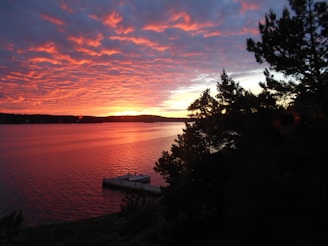 A vibrant sunset over a calm lake with a boat silhouette.