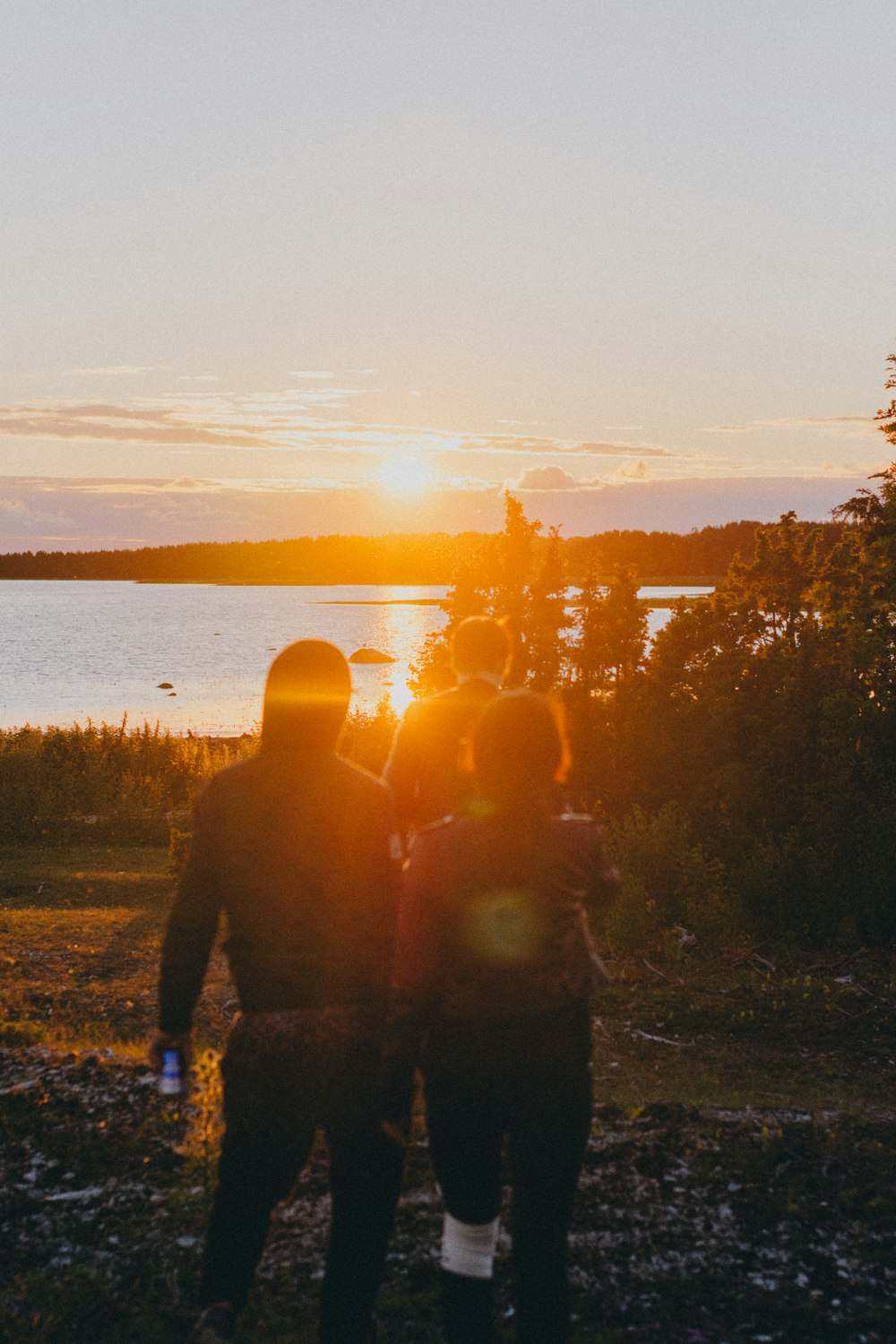 silhouette of people standing on ground near body of water during sunset