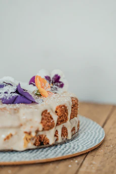Close-up of a rustic vegan cake decorated with fresh Andean flowers and natural ingredients on a wooden table.