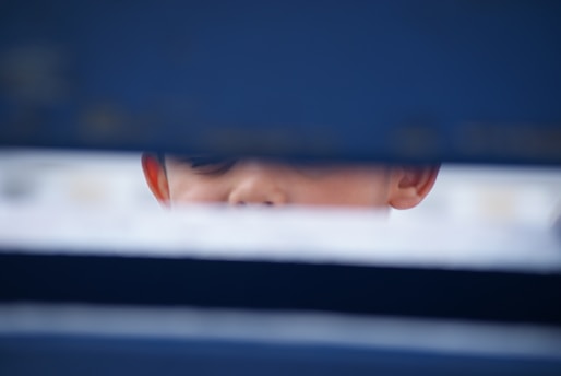 A child's face partially obscured by horizontal dark blue and light barriers, only showing the eyes and forehead.