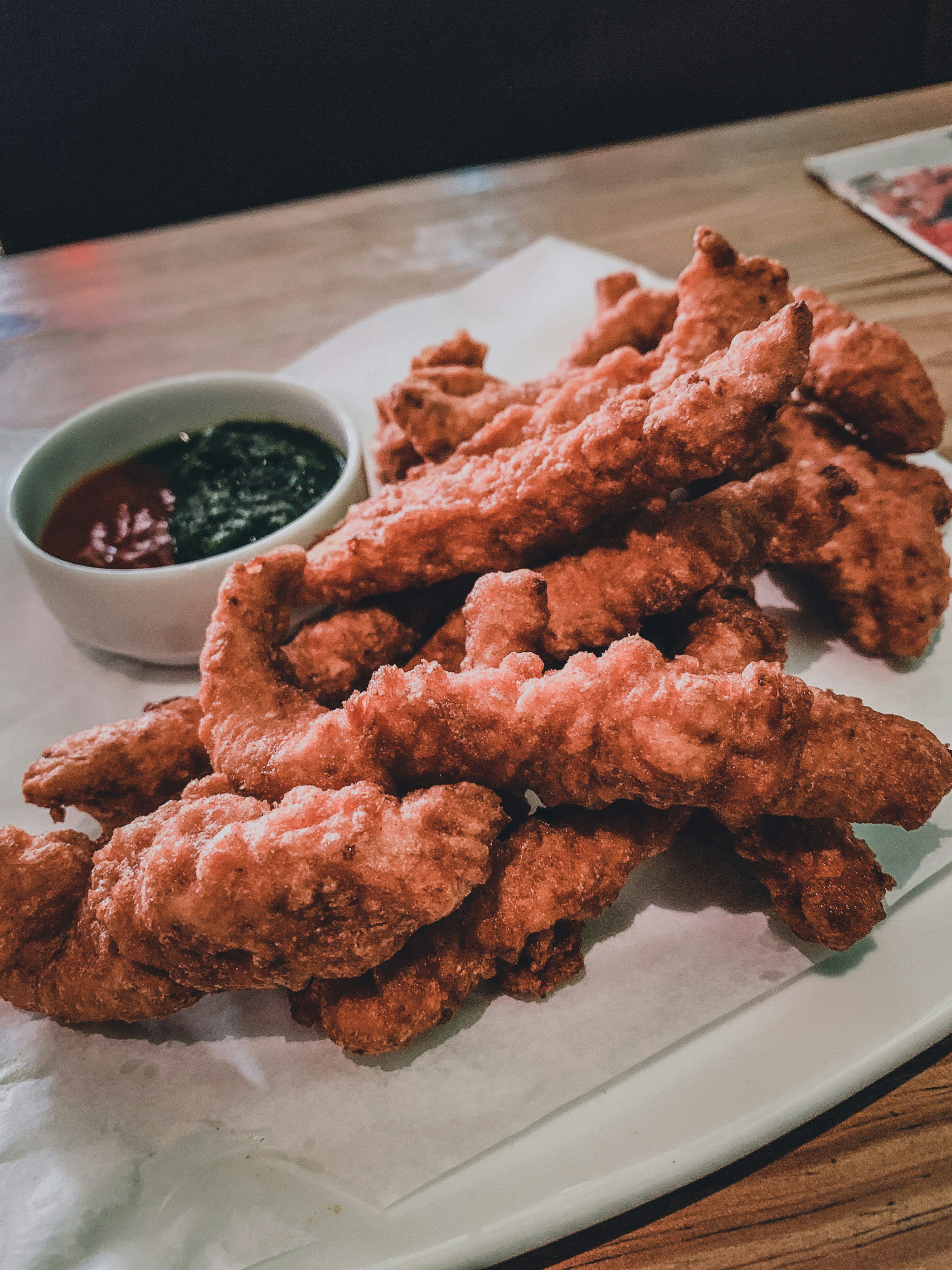 Fristiernos: cuatro tiras de pollo tierno apanado dorado crujiente sobre tabla de madera con salsas de acompañamiento