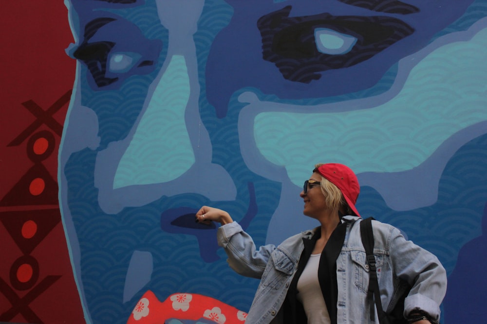 woman in gray denim jacket and red knit cap standing beside blue and white wall