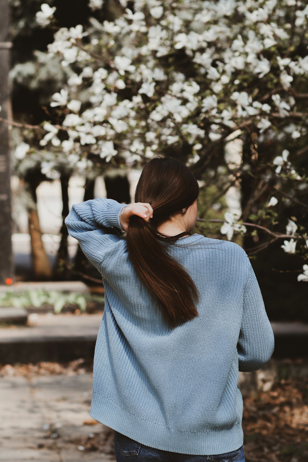 woman in gray sweater standing near trees during daytime