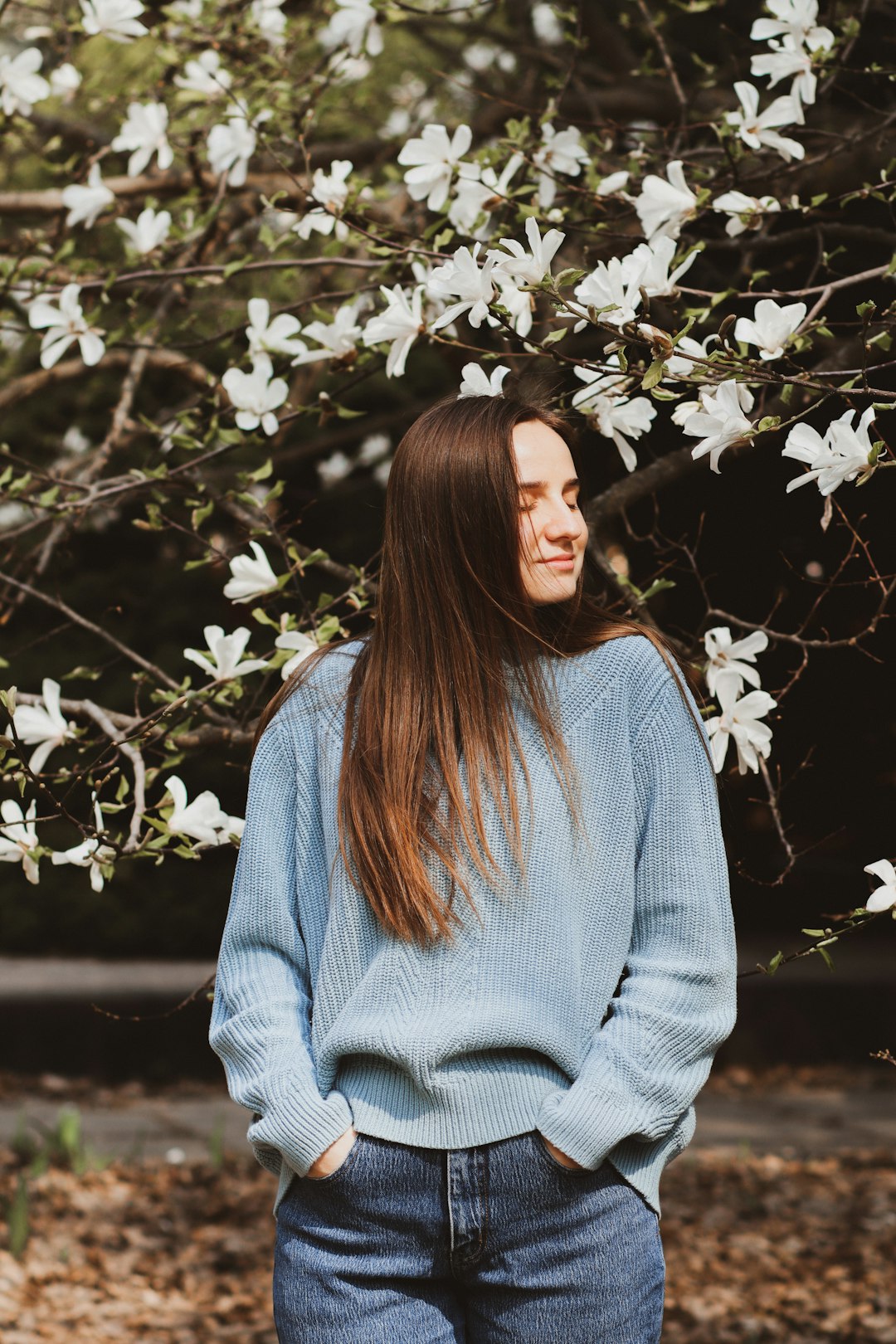 woman in gray sweater standing under white flowers