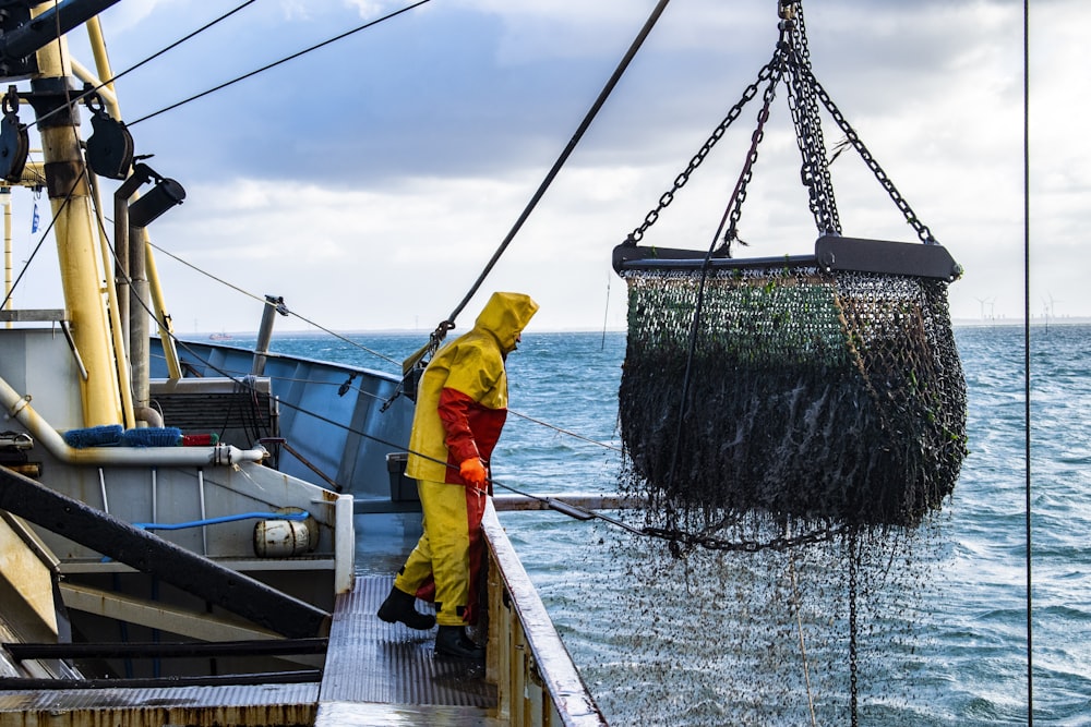 uomo in giacca gialla e pantaloni gialli in piedi sul molo della barca durante il giorno