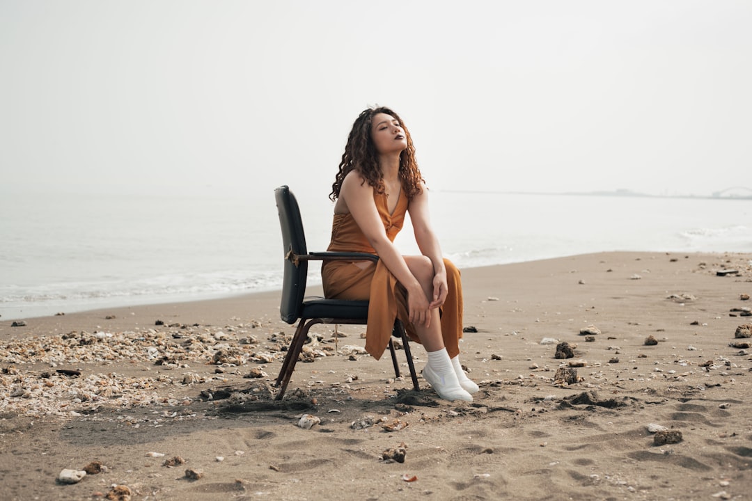 woman in white tank top sitting on black chair on beach during daytime