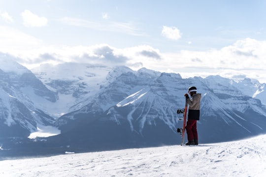 man in black jacket and blue denim jeans standing on snow covered ground during daytime in Lake Louise Mountain Resort Canada