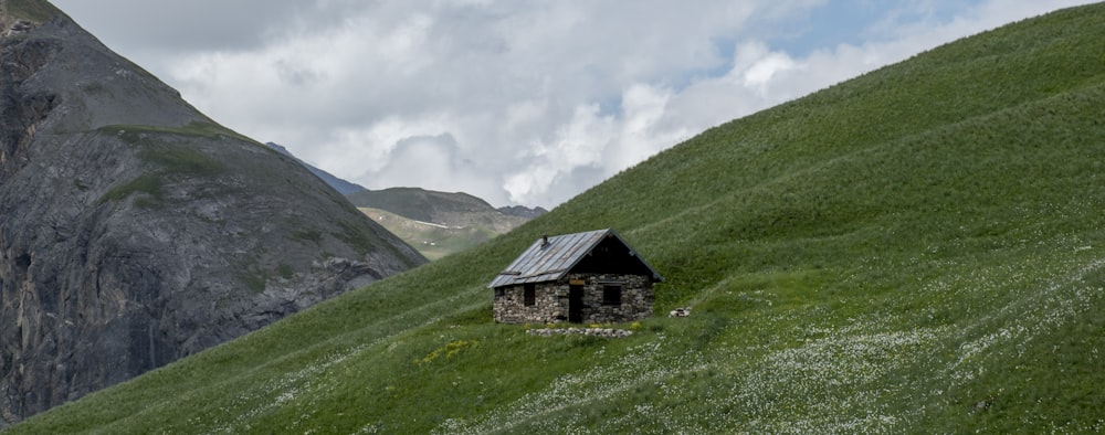 casa preta e cinza no campo de grama verde perto da montanha sob nuvens brancas durante o dia