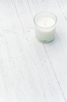 Elegant artisanal candle glowing warmly on a whitewashed wooden surface with minimalistic decor.