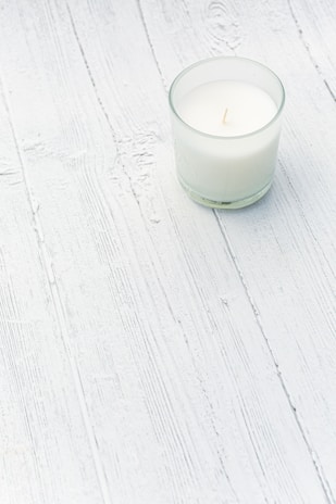 Close-up of a minimalist candle on a wooden table surrounded by soft natural light.
