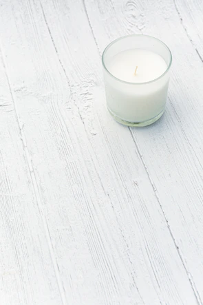 Elegant artisanal candle glowing warmly on a whitewashed wooden surface with minimalistic decor.