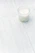 A serene, softly lit scene of a minimalist candle burning on a white marble surface beside a delicate ceramic vase.