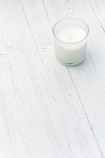 Close-up of a softly glowing Lumine Home scented candle in a minimalist white ceramic holder on a light wooden surface.