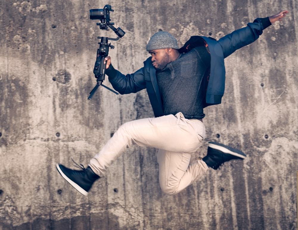 man in blue long sleeve shirt and white pants holding black and gray airsoft rifle