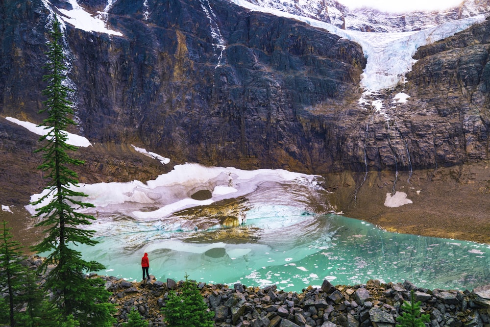 person in red shirt standing on rock near lake during daytime