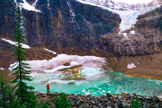 person in red shirt standing on rock near lake during daytime in Mount Edith Cavell Canada
