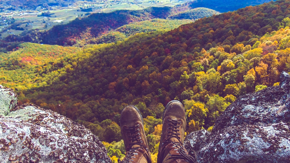 person in brown hiking boots sitting on rock formation during daytime