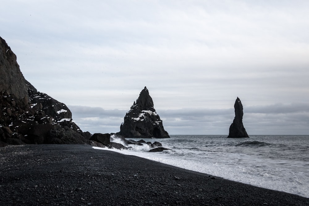 black rock formation on sea under white clouds during daytime