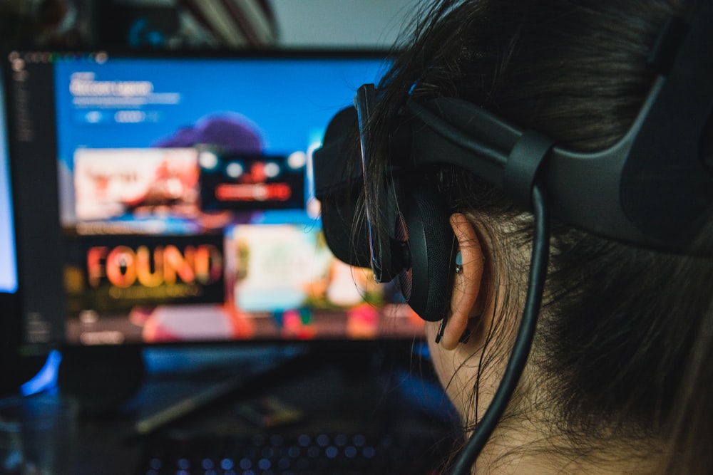 person wearing black headphones in front of black flat screen computer monitor