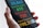 A hand holds a smartphone displaying a screen with colorful statistics related to health data. The numbers are large and prominent, with different colors assigned to each category for cases, recoveries, deaths, and suspicions.