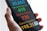 A hand holds a smartphone displaying a screen with colorful statistics related to health data. The numbers are large and prominent, with different colors assigned to each category for cases, recoveries, deaths, and suspicions.