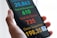 A hand holds a smartphone displaying a screen with colorful statistics related to health data. The numbers are large and prominent, with different colors assigned to each category for cases, recoveries, deaths, and suspicions.