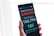 A hand holding a smartphone displaying COVID-19 statistics, showing total confirmed cases, total deaths, and the number of affected countries/regions. The screen has bold numbers and text in red, gray, and green against a black background.