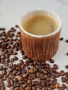 Freshly brewed coffee cup on a rustic wooden table surrounded by coffee beans.
