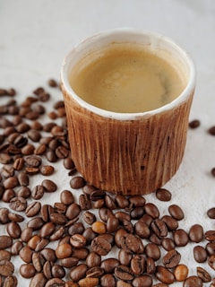 A steaming cup of blended coffee placed on a rustic wooden table, with coffee beans scattered around.