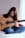 A person sitting cross-legged on a bed playing an acoustic guitar, focused on their music. The room has a soft ambiance with natural light filtering through a sheer curtain.