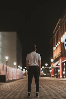 Mark standing alone on an empty city street at night, bathed in the warm glow of a streetlamp.