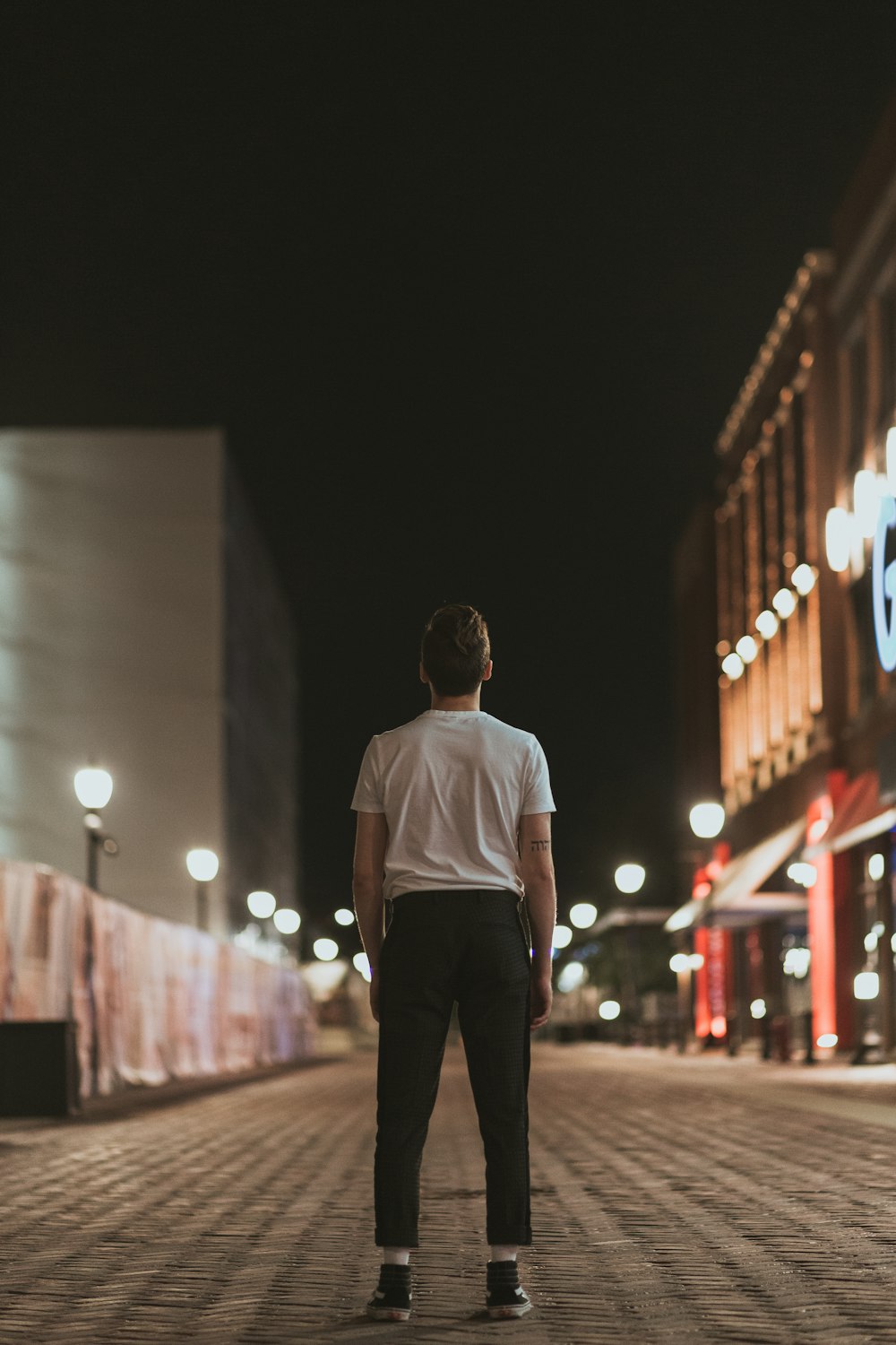 man in white crew neck t-shirt and black pants standing on street during night time