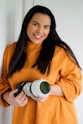 woman in orange sweater holding black and white camera