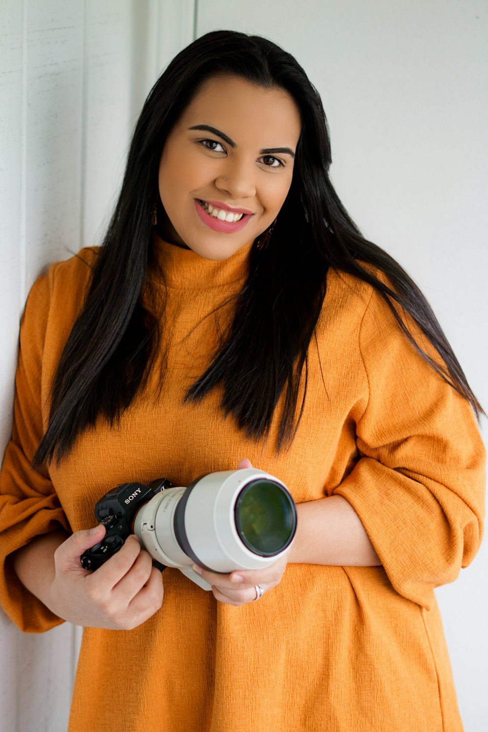 Femme en pull orange tenant un appareil photo noir et blanc