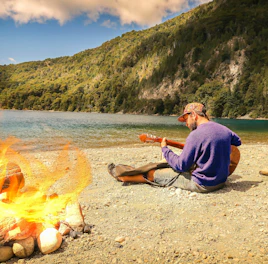 Musician recording native drums beside a mountain river under cloudy skies.