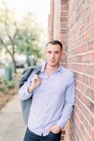 A man in a relaxed-fit shirt and jeans leaning against a rustic brick wall.