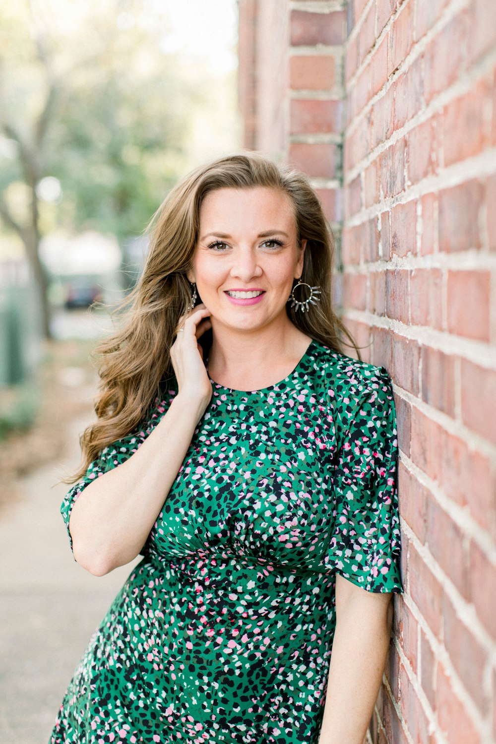 woman in blue and black floral dress leaning on brick wall