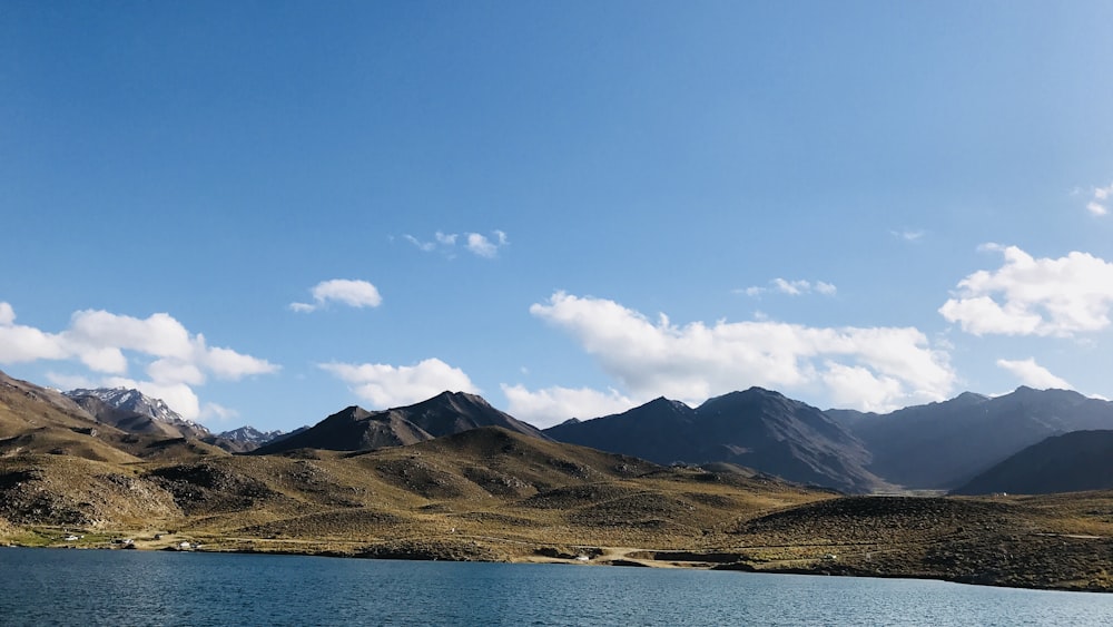 brown mountain near body of water under blue sky during daytime