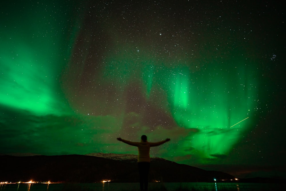 man standing on rock formation under green sky during night time