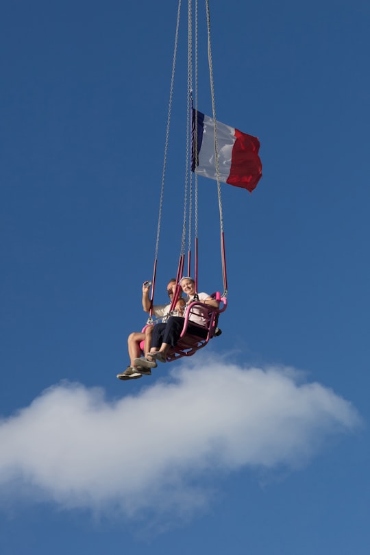 man in red shirt and black shorts riding on swing under blue sky during daytime in Tuileries France