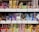 A variety of packaged snacks and treats are neatly displayed on grocery store shelves. The packaging features vibrant colors such as red, yellow, and blue, with labels in Japanese text. Each row on the shelves showcases different types of snacks, including both sweet and savory options.